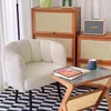 A cozy living room corner with a white armchair, a small side table, and wooden cabinets. Produktbild-Vorschau