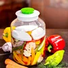A large glass jar filled with pickled vegetables, surrounded by fresh vegetables on a dark surface. Anteprima dell’immagine prodotto