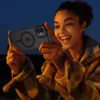 A young woman is holding an iPhone with a protective case and screen protector, smiling and looking at the phone. Produktbild-Vorschau