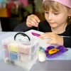 A young girl is engaged in a craft activity, using a needle and thread on a piece of paper, with a multi-tiered storage box filled with colorful craft supplies in the foreground. Produktbild-Vorschau
