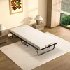 A folding bed with a mattress is set up on a rug in a room with a painting on the wall and a window view of greenery. Voir les images du produit