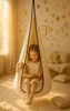 A young girl is sitting in a hanging chair, reading a book. The room is decorated with star-shaped lights. Produktbild-Vorschau