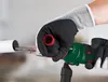 A person wearing gloves is using a green power tool to work on a white pipe. Produktbild-Vorschau