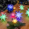 A string of star-shaped LED lights is arranged on a wooden surface with pine branches and pinecones. Produktbild-Vorschau