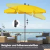 A yellow patio umbrella is shown tilted and at different heights on a deck overlooking the ocean, with two wicker chairs and ottomans in the foreground. Produktbild-Vorschau
