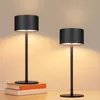 Two black table lamps are displayed on a wooden surface, with one lamp placed on top of two books. Náhľad obrázku produktu