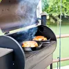 Two cast iron pans with food cooking on a grill, with smoke rising. Voir les images du produit