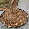 A garden bed border surrounding a tree trunk, covered in bark chips, with gravel paths on either side. Produktbild-Vorschau