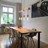 A dining room with a wooden table and chairs, illuminated by a wooden pendant light fixture. Anteprima dell’immagine prodotto
