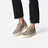 A pair of leopard print sneakers worn by a person wearing black jeans. Voir les images du produit