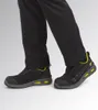 A person wearing black pants and black safety shoes with yellow accents. Produktbild-Vorschau