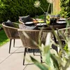 An outdoor dining set with chairs and a table, set on a patio with a garden in the background. Produktbild-Vorschau