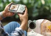 A person is holding a baby monitor that shows a sleeping baby. A separate camera unit is shown in the foreground, with a crib in the background. Náhľad obrázku produktu