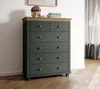A chest of drawers with a wooden top, placed against a white wall with a framed picture and a vase of flowers on top. Curtains are visible in the background. Podgląd zdjęcia produktu