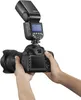 A person's hands are holding a DSLR camera with a flash unit attached to the hot shoe. Podgląd zdjęcia produktu