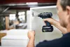 A person is using a cordless drill to attach a cabinet hinge to a white cabinet in a workshop. Produktbild-Vorschau
