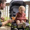 A father is feeding a pretzel to his baby who is sitting in a stroller. Voir les images du produit