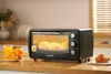 A mini oven with muffins baking inside, placed on a kitchen counter next to orange juice, an orange, and some toast. Náhľad obrázku produktu