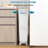 A white trash can is shown placed between a kitchen cabinet and a refrigerator, highlighting its slim design. Voir les images du produit
