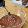 A hand mixer is shown mixing chocolate batter in a glass bowl, with muffins in the background. Produktbild-Vorschau