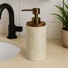 A soap dispenser sits on a bathroom counter next to a sink and a plant. Podgląd zdjęcia produktu