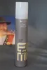 A Wella EIMI Glam Hair Mist bottle is shown against a gray background, with a blurred image of a person in the background. Podgląd zdjęcia produktu