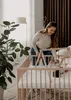 A mother is interacting with her baby in a wooden crib. Produktbild-Vorschau