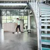 A woman is vacuuming a large, modern office space with a reception desk and a staircase. Produktbild-Vorschau