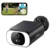 A security camera with a solar panel on top, shown next to a smartphone displaying a live feed of a park scene with people and a dog. Produktbild-Vorschau