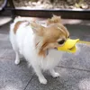A small dog wearing a yellow duck-billed muzzle stands on a paved surface. Produktbild-Vorschau