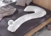 A white, C-shaped pillow is laid out on a dark gray bedsheet, with other pillows and a blanket visible in the background. Produktbild-Vorschau