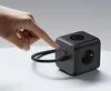 A hand is pressing a button on a black cube-shaped power strip. Produktbild-Vorschau