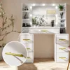 A white vanity table with a lighted mirror and gold handles, set in a room with a plant. Náhled obrázku produktu