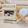 A wooden toy dishwasher and accessories are displayed on a patterned rug, with a wooden crib in the background. Voir les images du produit