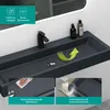 A close-up view of a modern, dark gray rectangular washbasin with a black faucet, set against a white tiled wall and a mirror. Produktbild-Vorschau