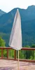 A closed umbrella stands on a wooden deck with a mountain and forest in the background. Produktbild-Vorschau