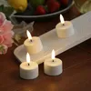 Four LED tea lights with a charging station are arranged on a wooden surface, with some flowers and fruit in the background. Produktbild-Vorschau