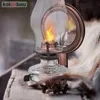 A vintage oil lamp with a flame sits on a wooden surface next to a furry material and a pinecone. Podgląd zdjęcia produktu