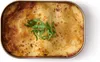 A close-up overhead view of a baked dish in a metal container, garnished with a sprig of green leaves. Podgląd zdjęcia produktu