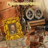 A collection of vintage items including framed portraits, books, and drinks on a wooden surface. Produktbild-Vorschau