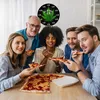 A group of friends are gathered around a table, enjoying pizza and drinks. A clock with a cannabis leaf design is visible on the wall. Produktbild-Vorschau