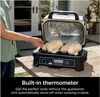 A person is using a Ninja Woodfire Pro XL grill outdoors, with two chickens cooking inside. The grill has its lid open, revealing the cooking area and a built-in fan. A thermometer probe is inserted into one of the chickens. Text overlays describe the 'Bui Voir les images du produit