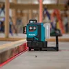 A Makita laser level is shown in a construction setting, projecting a red laser line onto a wooden plank. Produktbild-Vorschau