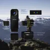 A mini body camera with various features labeled, set against a blurred mountainous background with a person in the midground. Produktbild-Vorschau