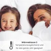 A mother and daughter are lying in bed, smiling and covered by white bedding. Produktbild-Vorschau