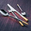 A set of cutlery with silver and gold accents arranged on a wooden surface. Produktbild-Vorschau