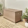 A beige polyrattan garden storage box is shown on a wooden deck next to a white brick wall and some plants. Anteprima dell’immagine prodotto