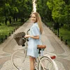 A woman is standing with her bicycle on a paved path in a park. Produktbild-Vorschau