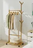 A wooden garment rack with clothes hanging on it, placed in a room with a dresser and a lamp. Produktbild-Vorschau