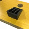 A close-up view of a black rubber foot with grooves, placed on a light brown wooden surface with visible grain. Two circular indentations are visible in the background. Náhled obrázku produktu